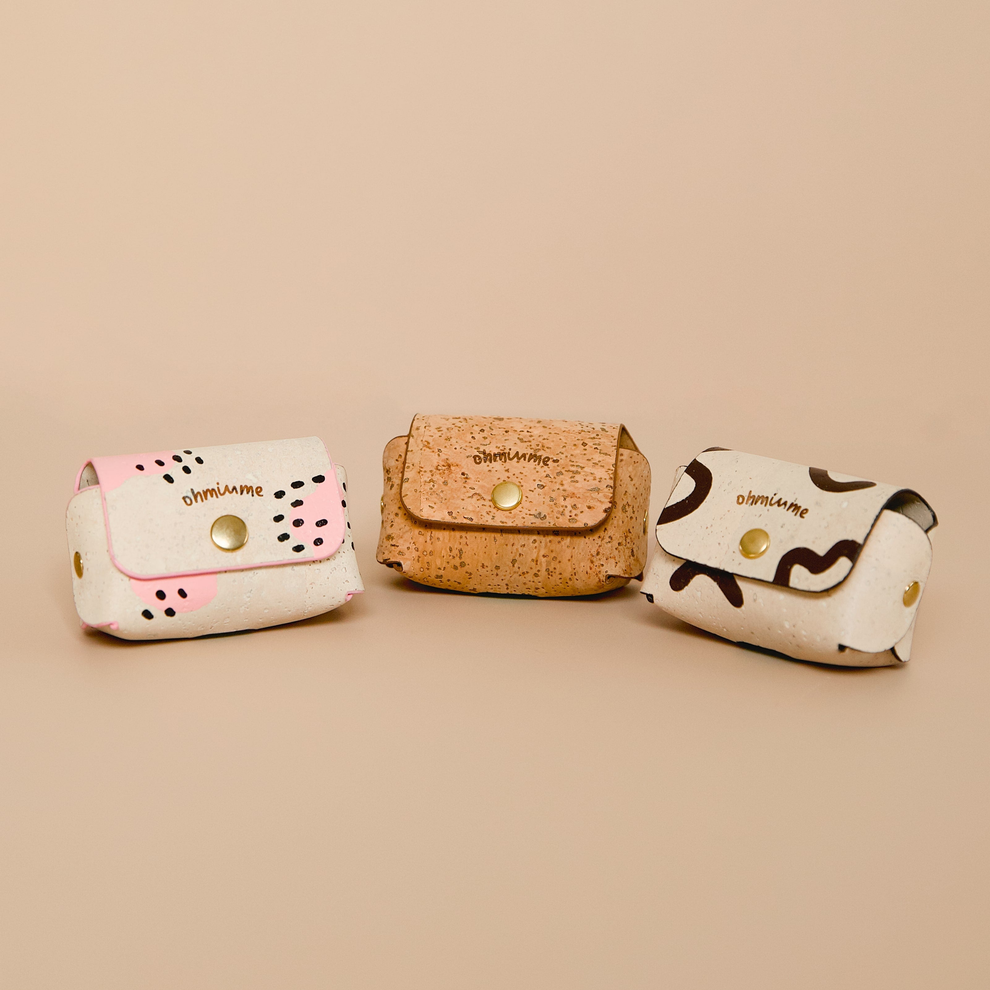 Three cork leather dog poop bag holders with hand-painted details in brown tan and cream beige