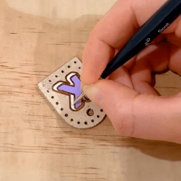 Hand holding a brush painting a dog name tag in purple on cream beige cork leather