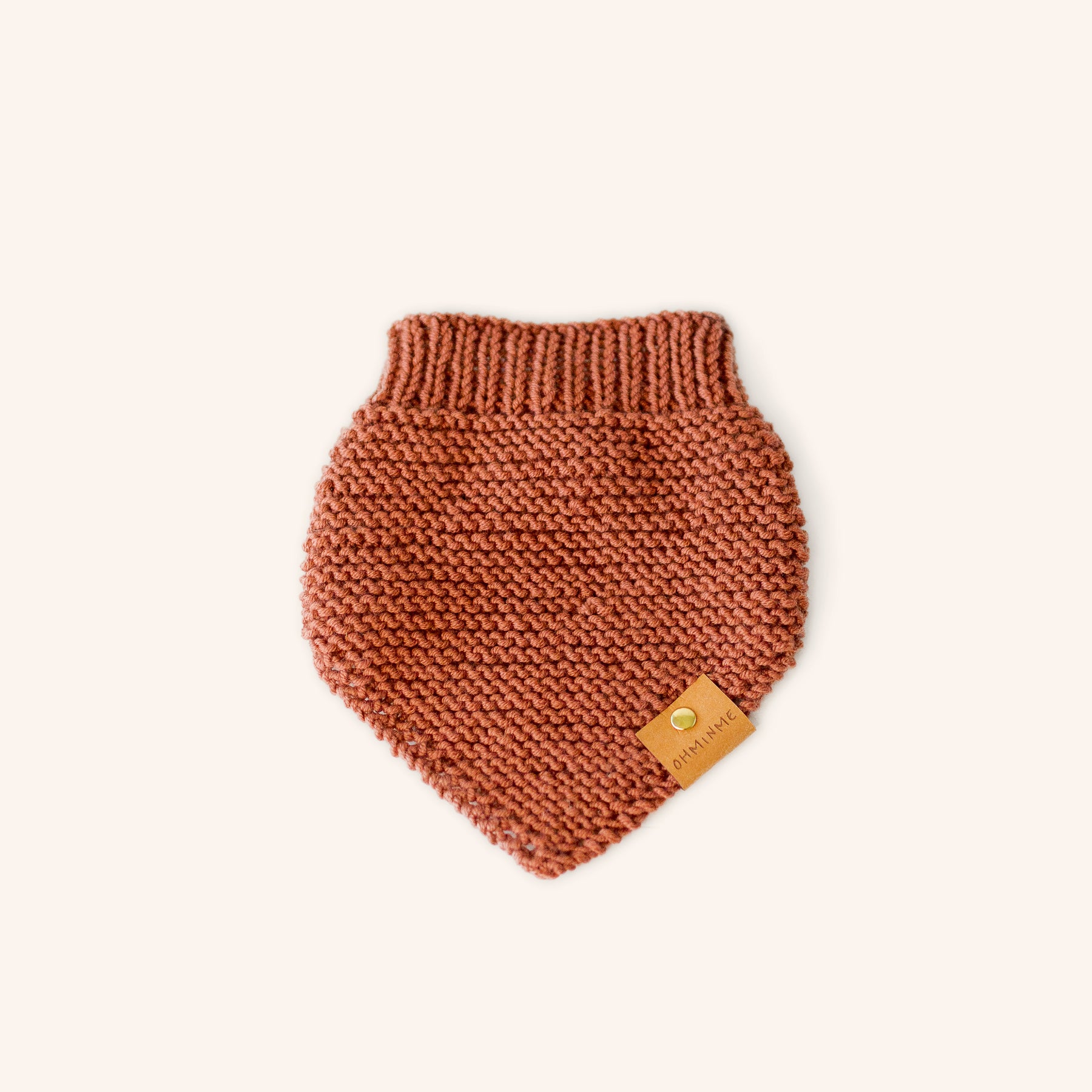 knitted pet bandana in a rusty dark orange colour with a paper label and brass rivet
