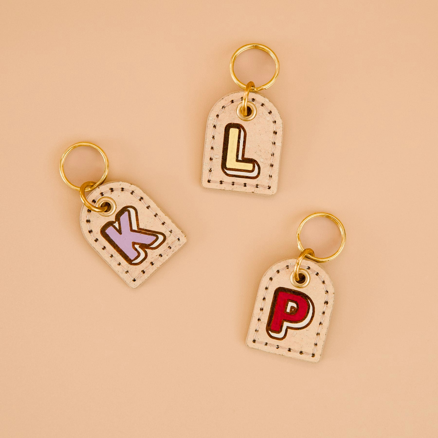 Three beige cork leather dog ID tags with painted edges, personalised monogram, brass split rings