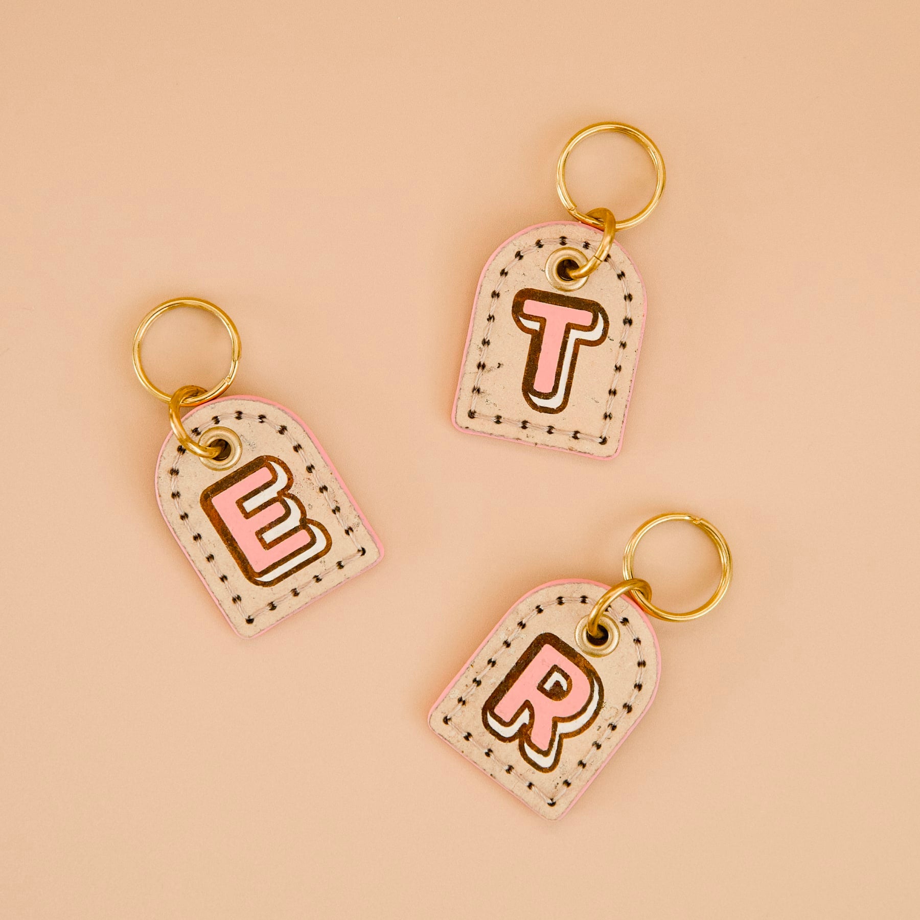 Three beige cork leather dog ID tags with pink painted edges, personalised monogram, brass split ring