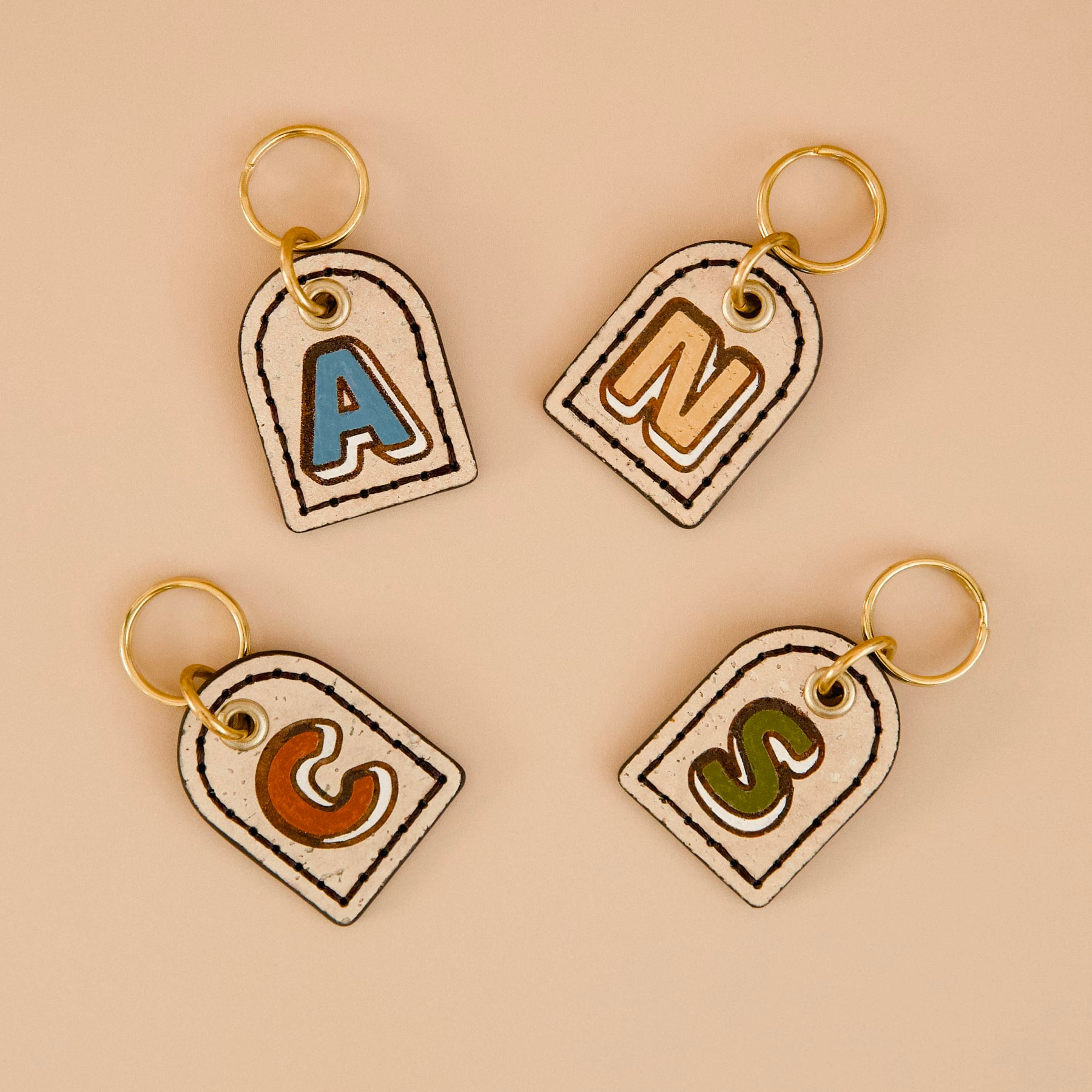 Four beige cork leather dog ID tags with dark espresso painted edges, personalised monogram, brass split ring