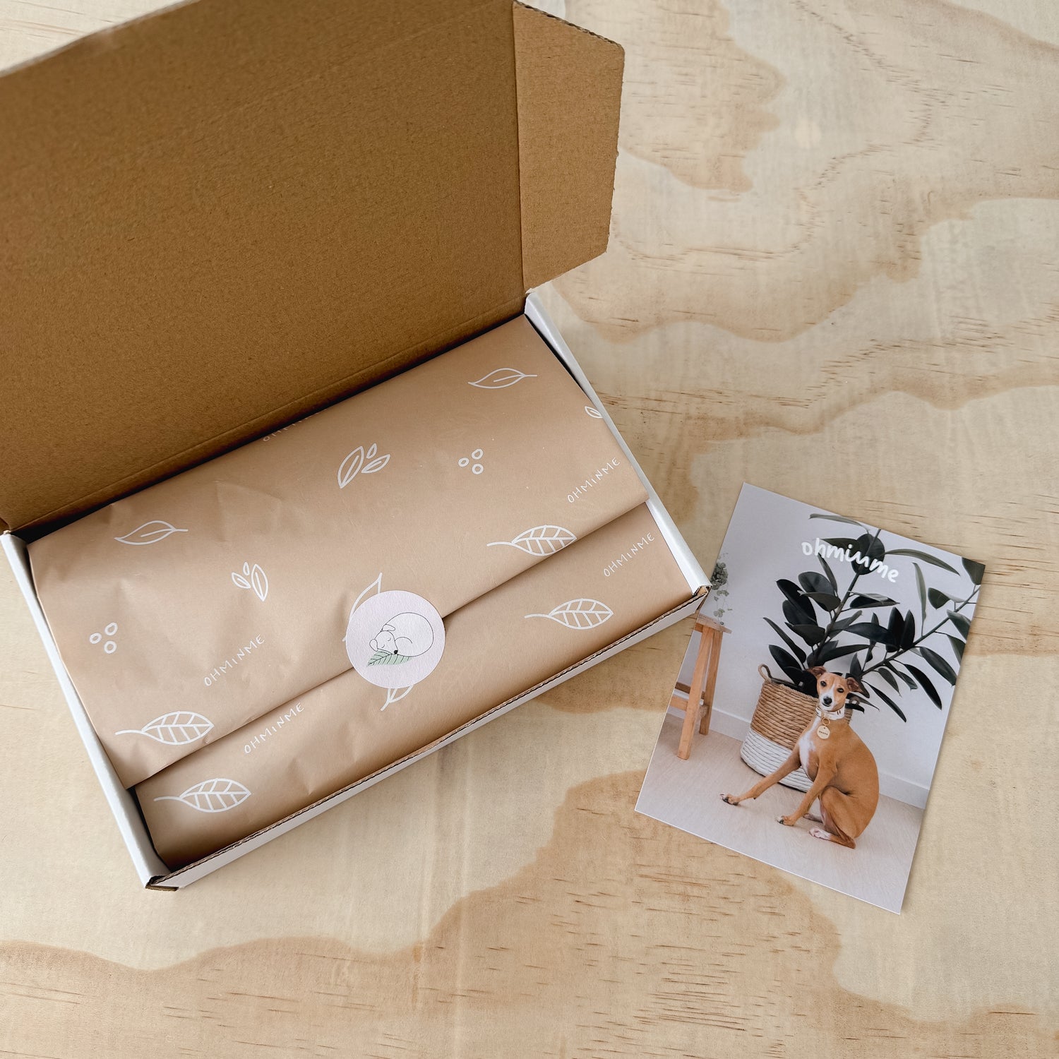 Ohminme box with an order wrapped in branded tissue paper and a thank you card placed beside it