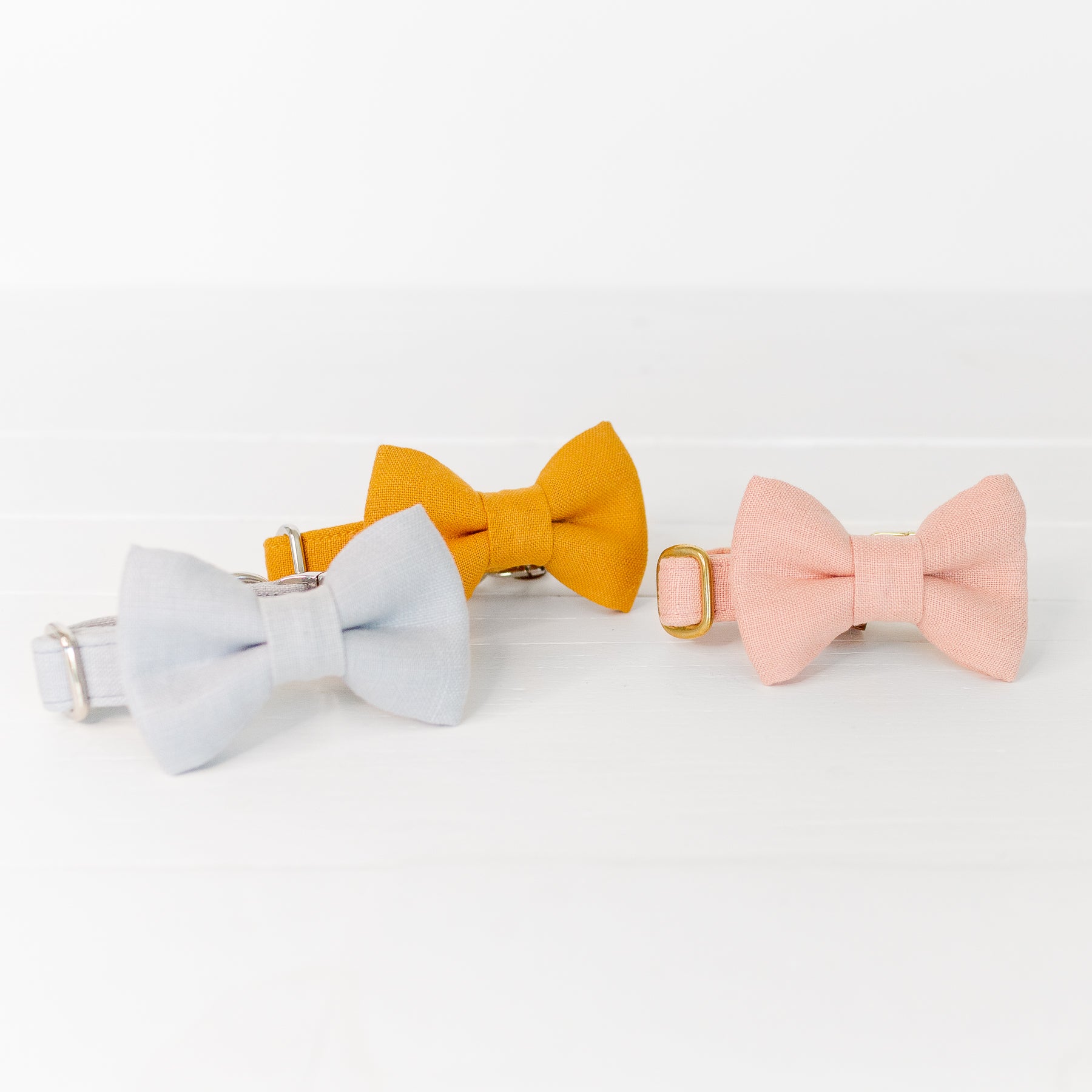 Three linen dog collars with matching bow ties in sky blue, mustard yellow, and soft pink.
