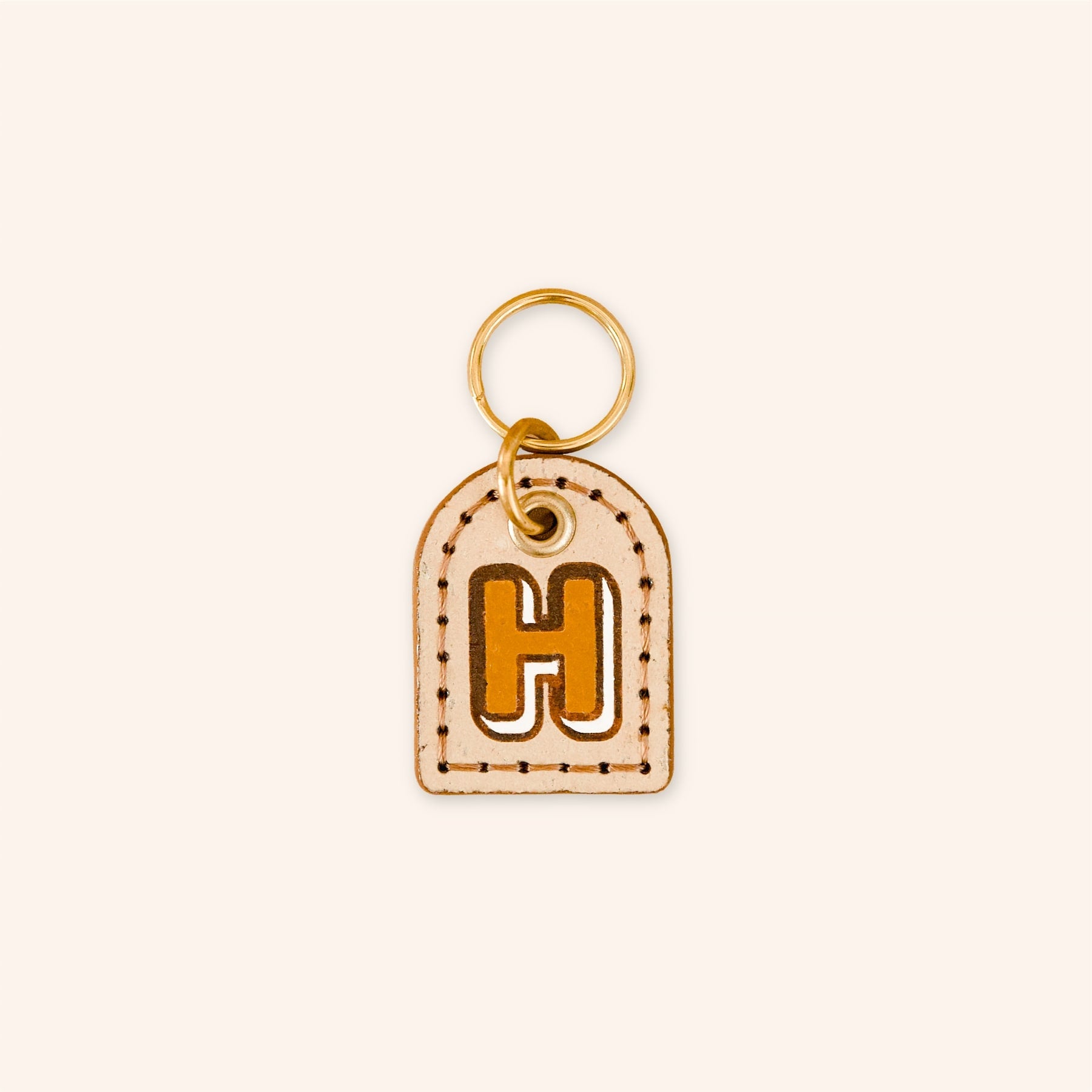 Custom dog tag with letter 'H' in tan on beige cork leather.