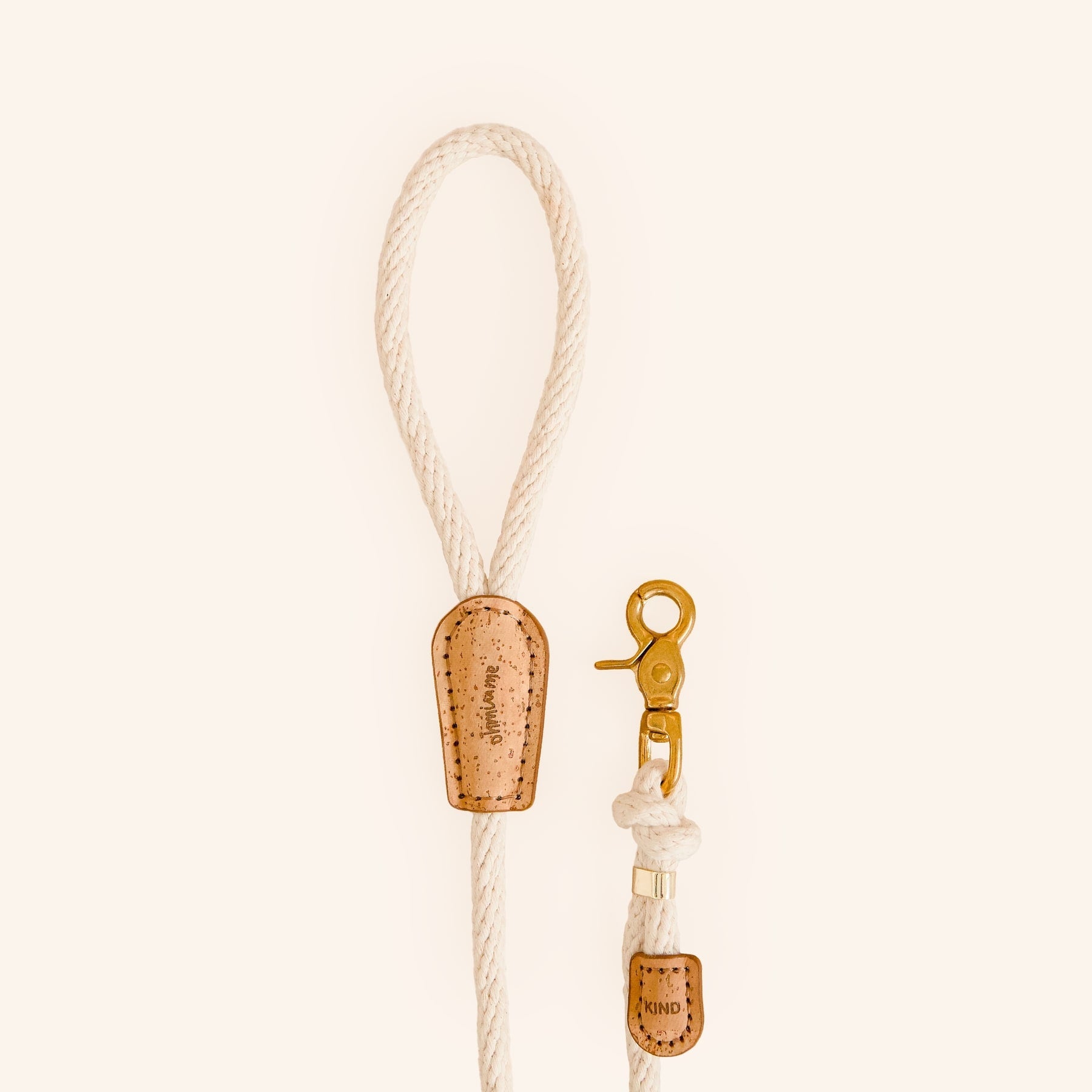 White cotton rope dog leash with brown cork details and brass snap, "be kind" engraved.