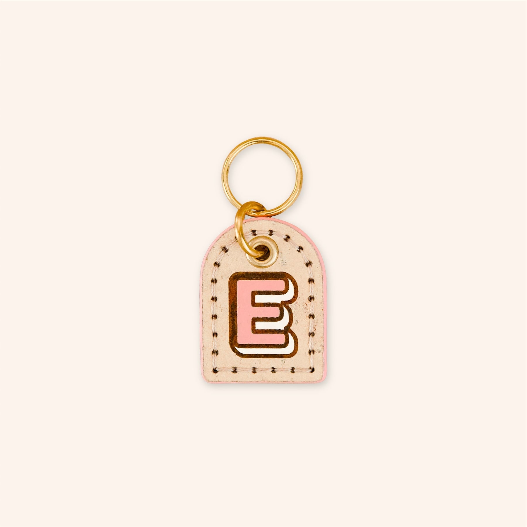 Custom dog ID tag with letter 'E' in pink on cream cork leather.