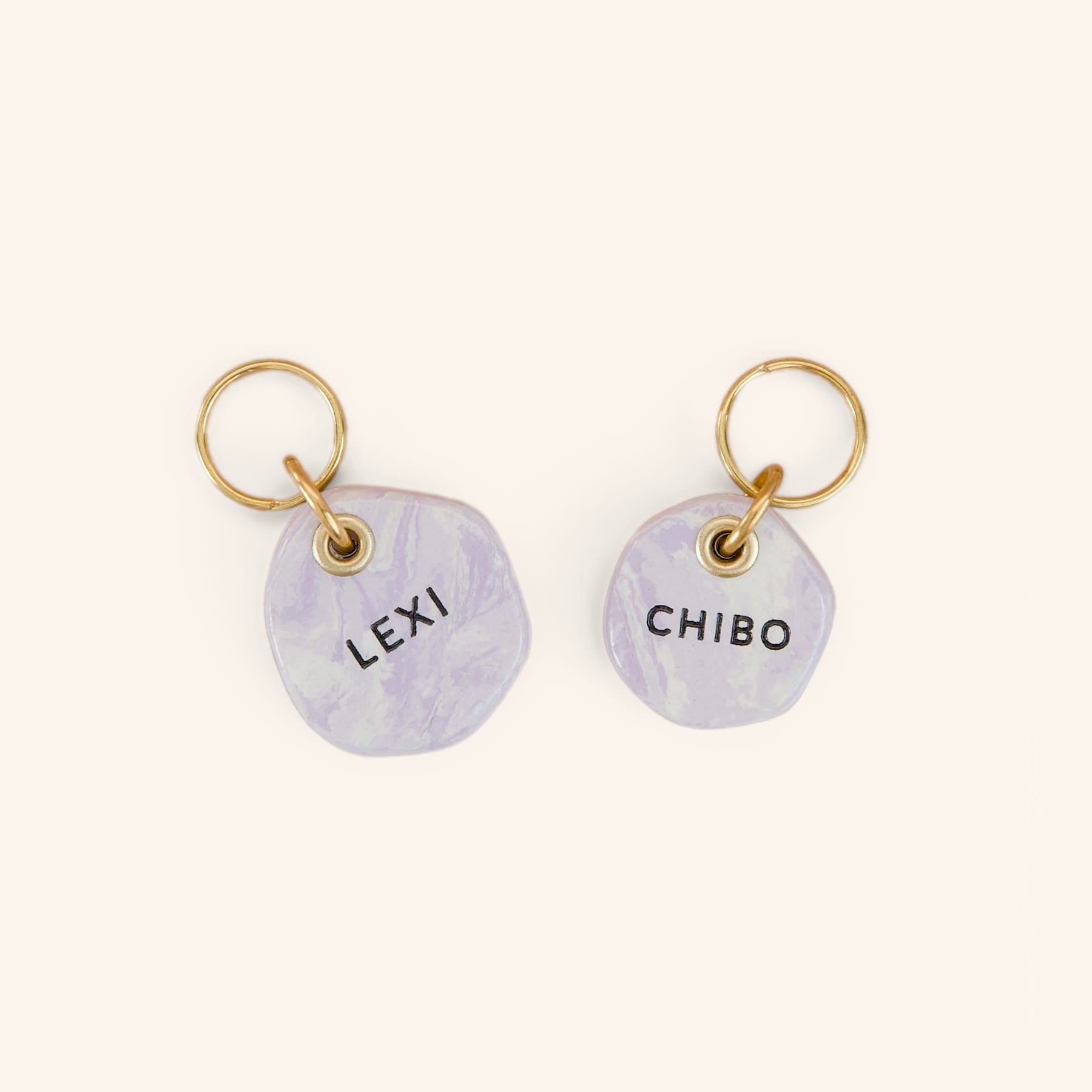 Two personalised dog ID tags in purple engraved with “Lexi” and “Chibo”, with brass split rings