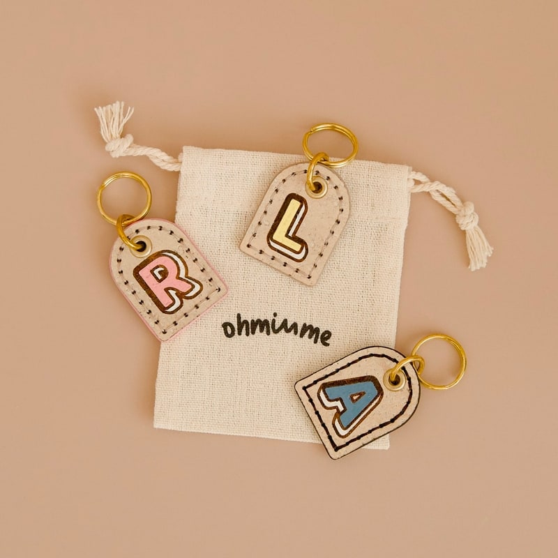 Personalised dog name tags with letters R, L, and A, on a linen drawstring bag