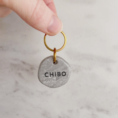 hand holding a customized handmade dog ID tag with marble look, featuring the name 'Chibo' on the front